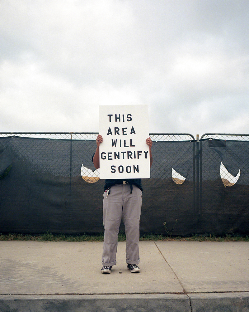 Artist holding a sign in front of a fence