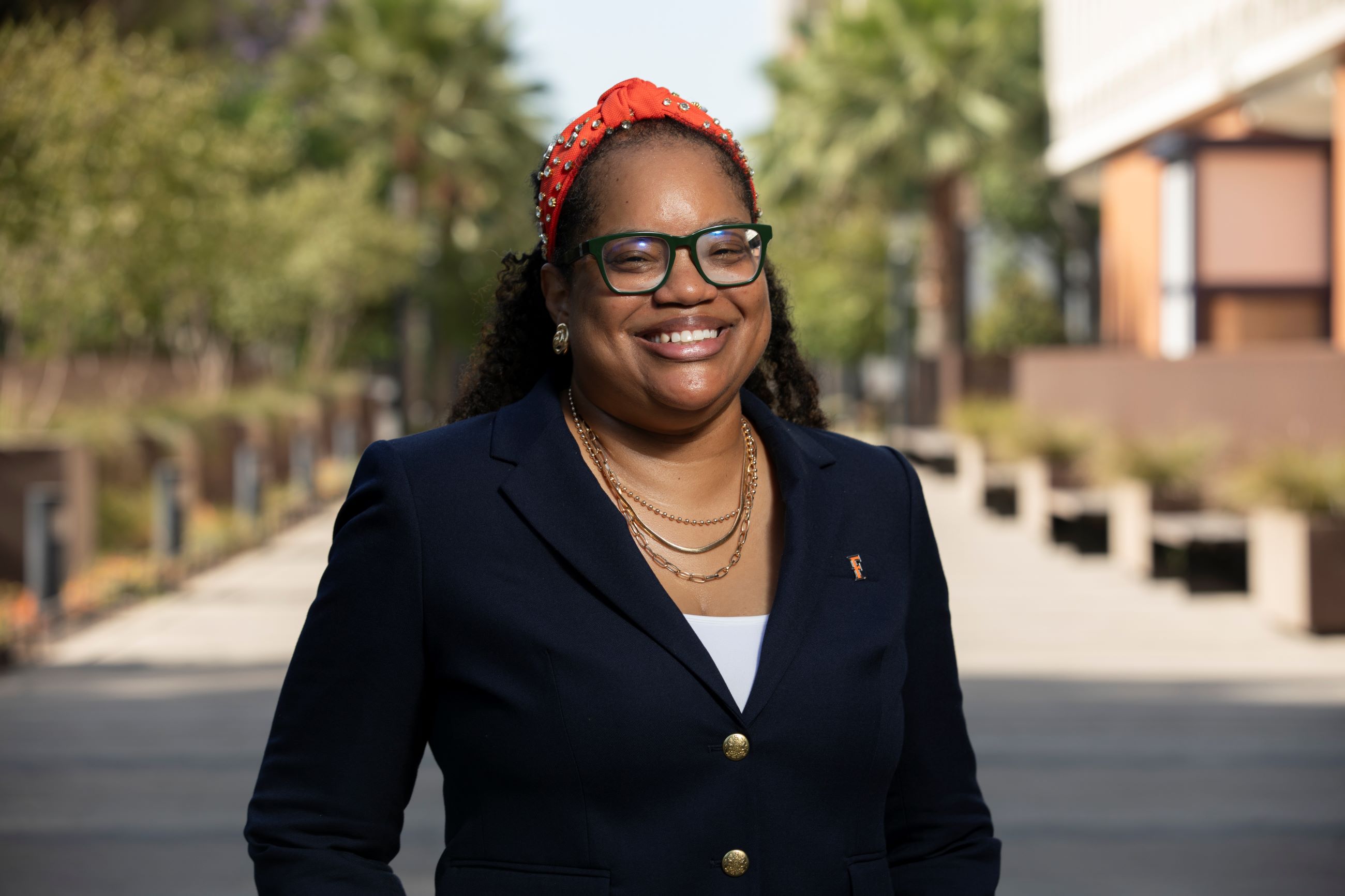 Headshot of a person standing in front of CSUF Titan Walk, wearing professional attire, with a confident expression