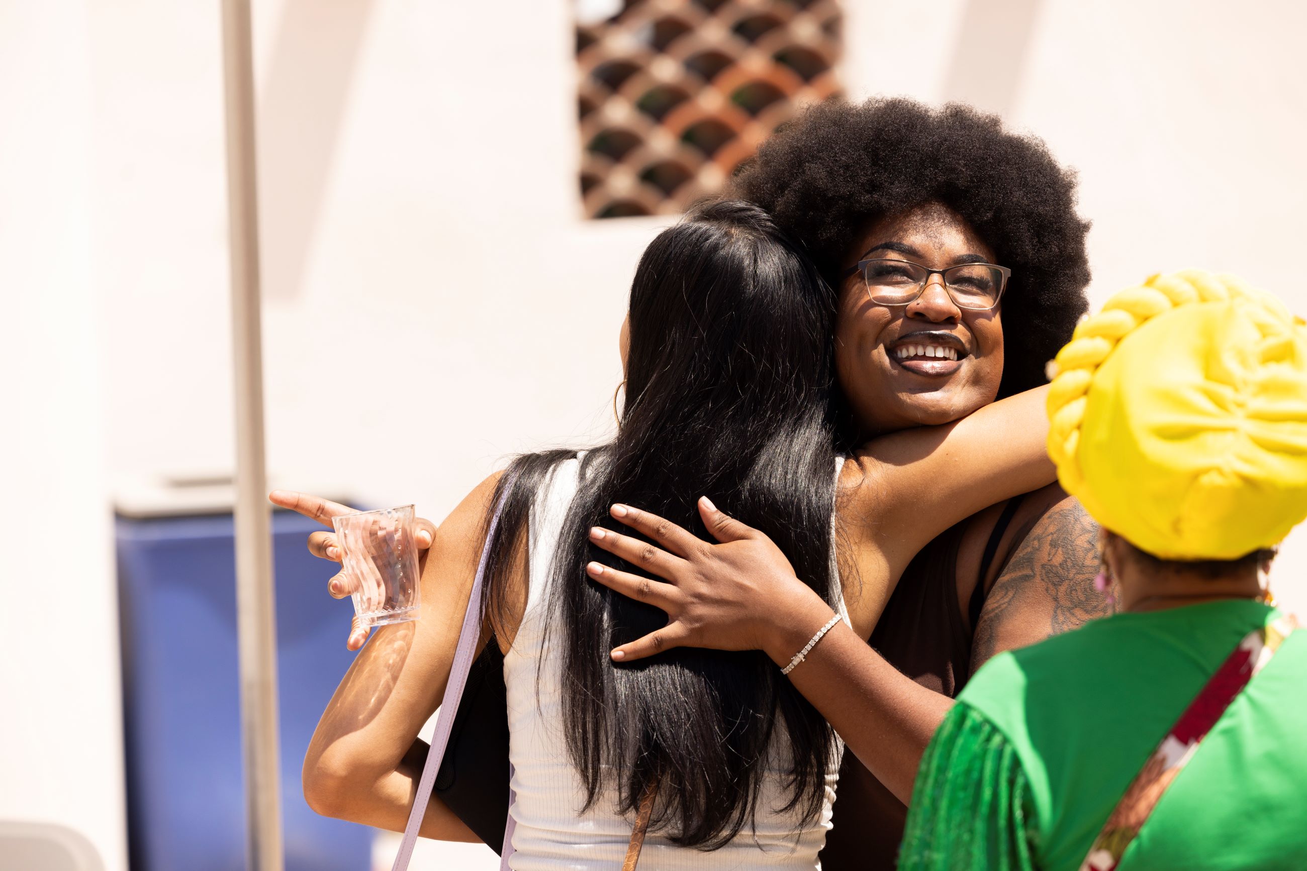 Two women in a group of three happily hugging while at a social event 