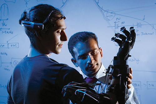 Student trying on prototype of mechanical hand with professor overlooking