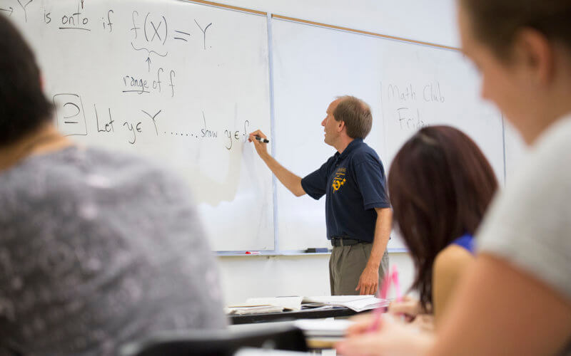 Dr. Annin writes on whiteboard in a math class.