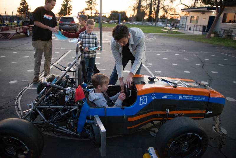 CSUF student helping a child get ready in a racecar