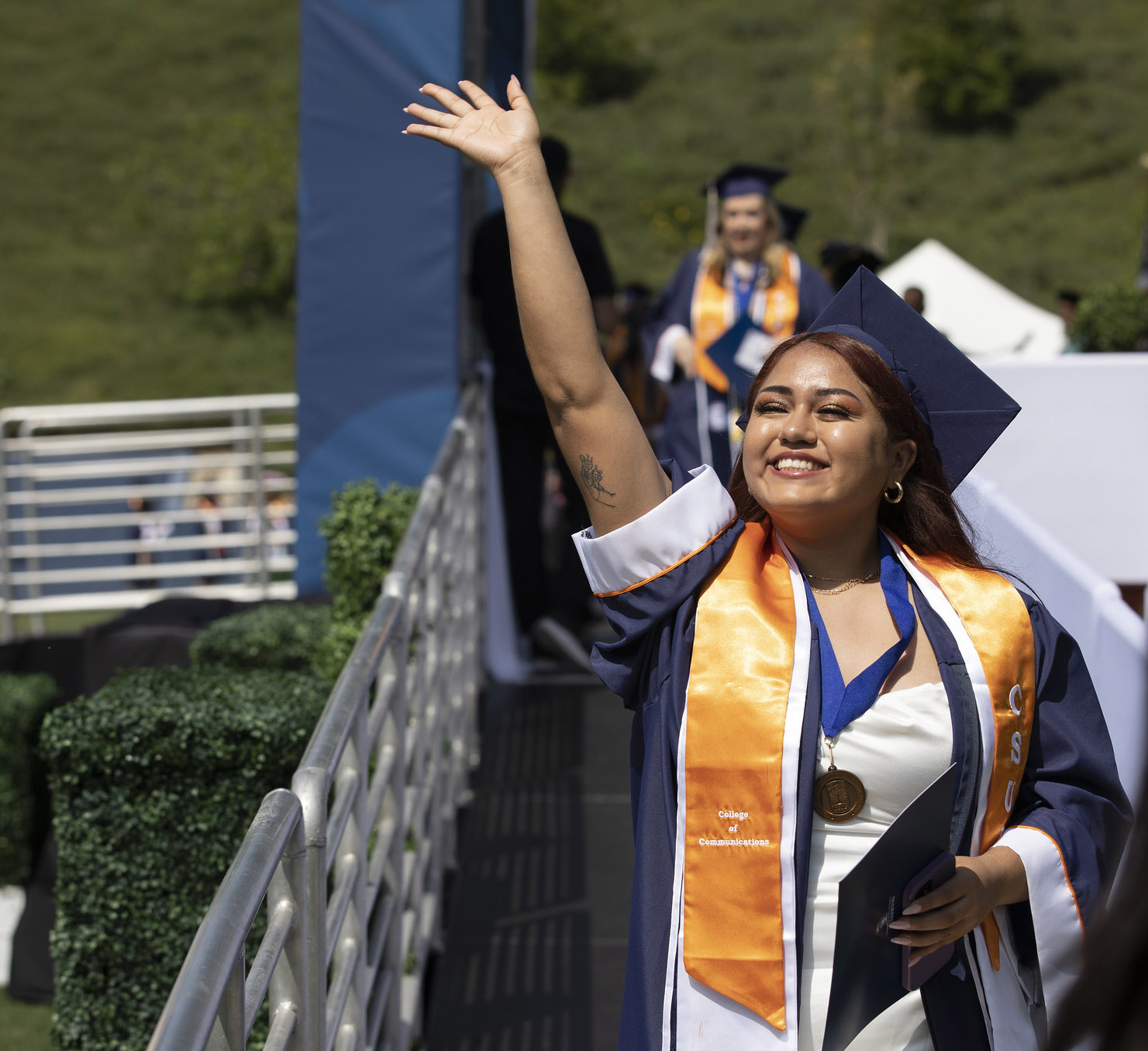 Latina student waves at crowd as she walks offstage after receiving her diploma during commencement.