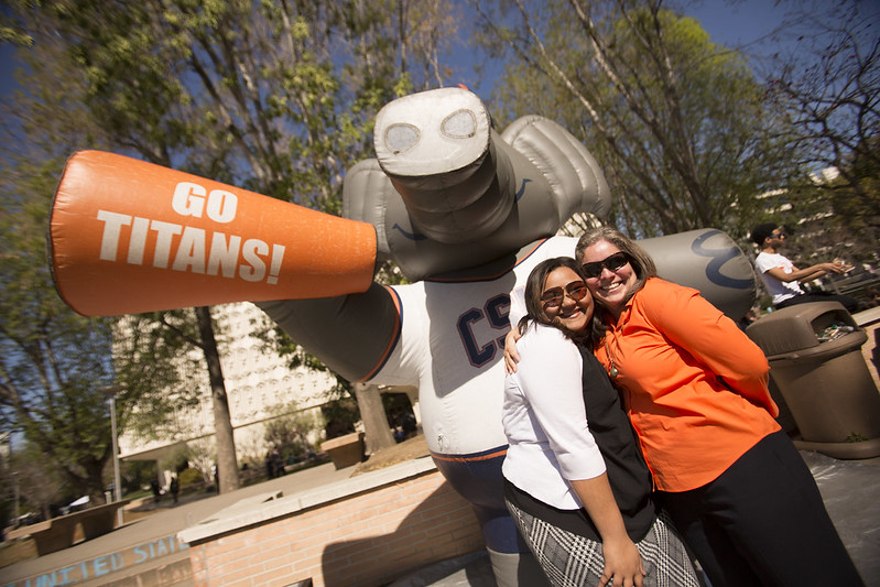 Two staff members pose in front of Tuffy Titan inflatable that has an airhorn saying "GO TITANS!".