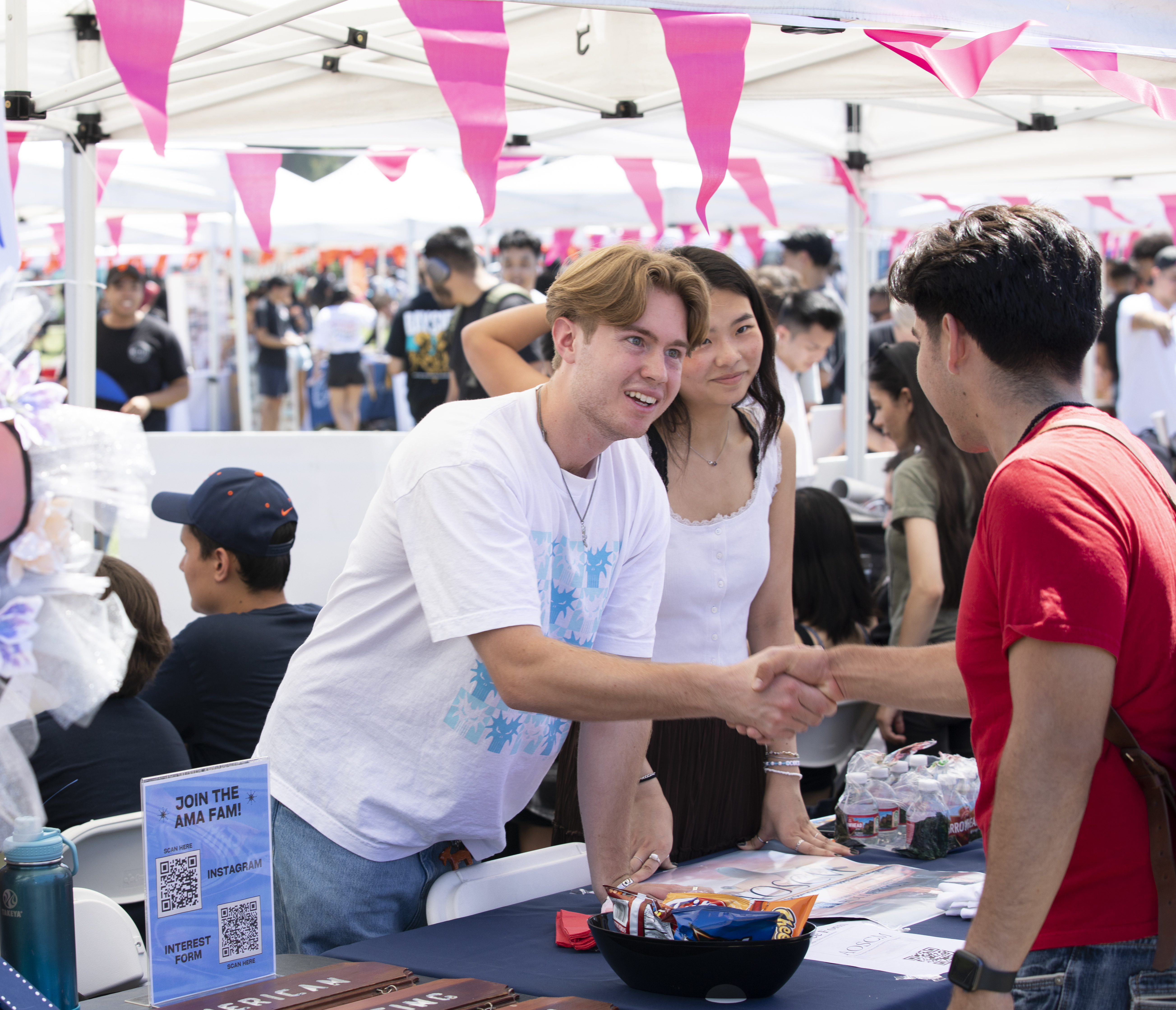 Students with the American Marketing Association meet a prospective club member at Discoverfest in Fall 2023. They shake each other's hands as they meet one another.