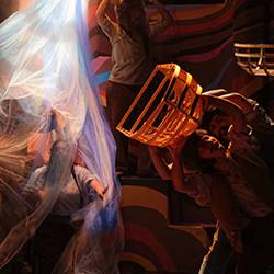 Stage actors carrying model boats through diaphonous fabric.
