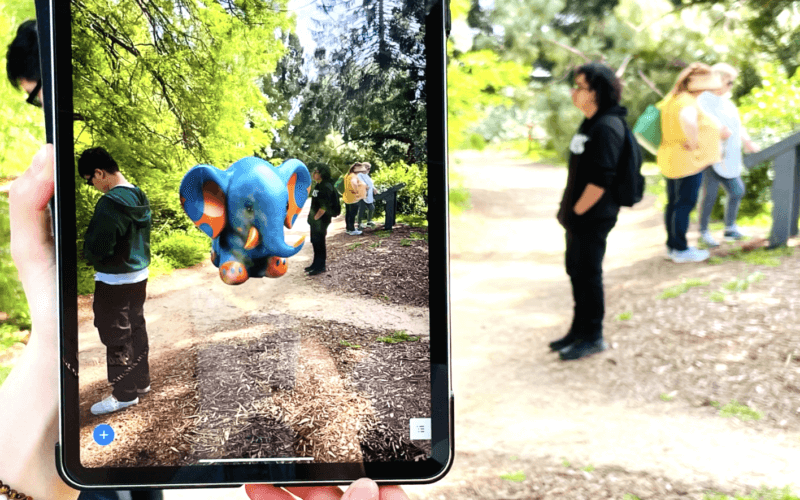 Hand holding smartphone with augmented reality elephant displayed.