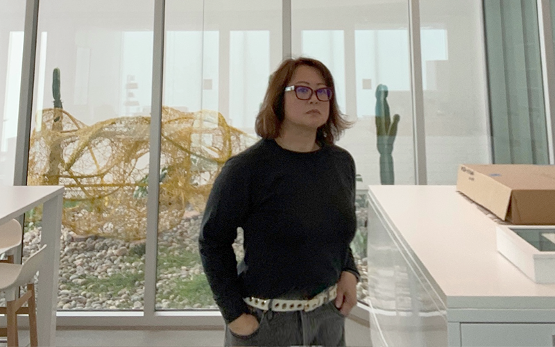 Woman standing in a room near a large window.