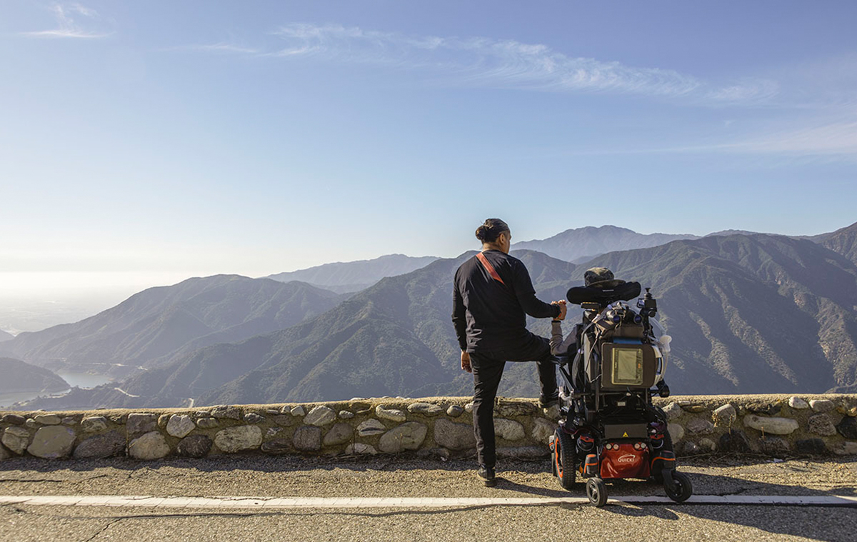 Two people facing a scenic hillside, holding hands.