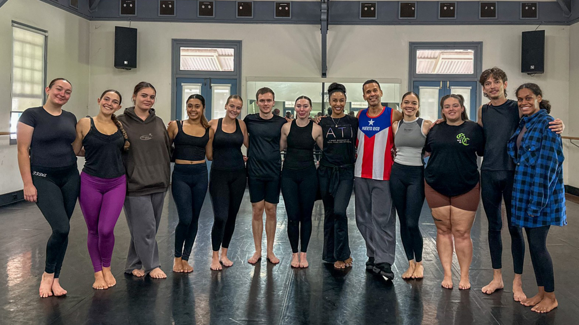 Men and women standing together in a dance rehearsal space.