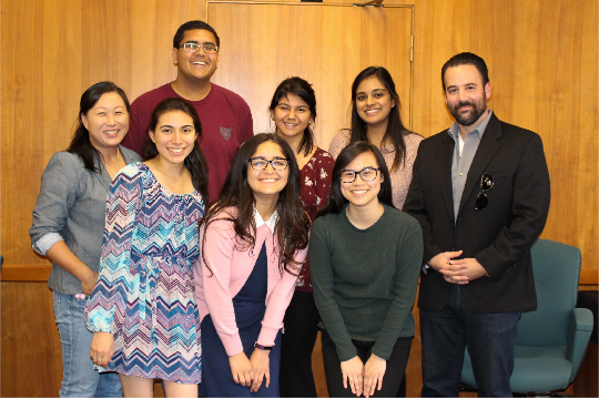 A group of college students and two program advisors smile in a classroom