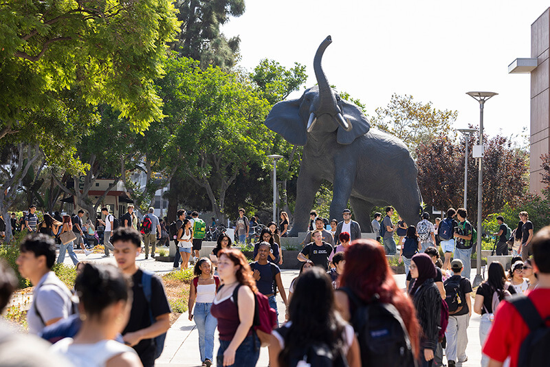Students walk through a busy campus plaza as the Titan the Elephant statue rises above the walkway at California State University, Fullerton.