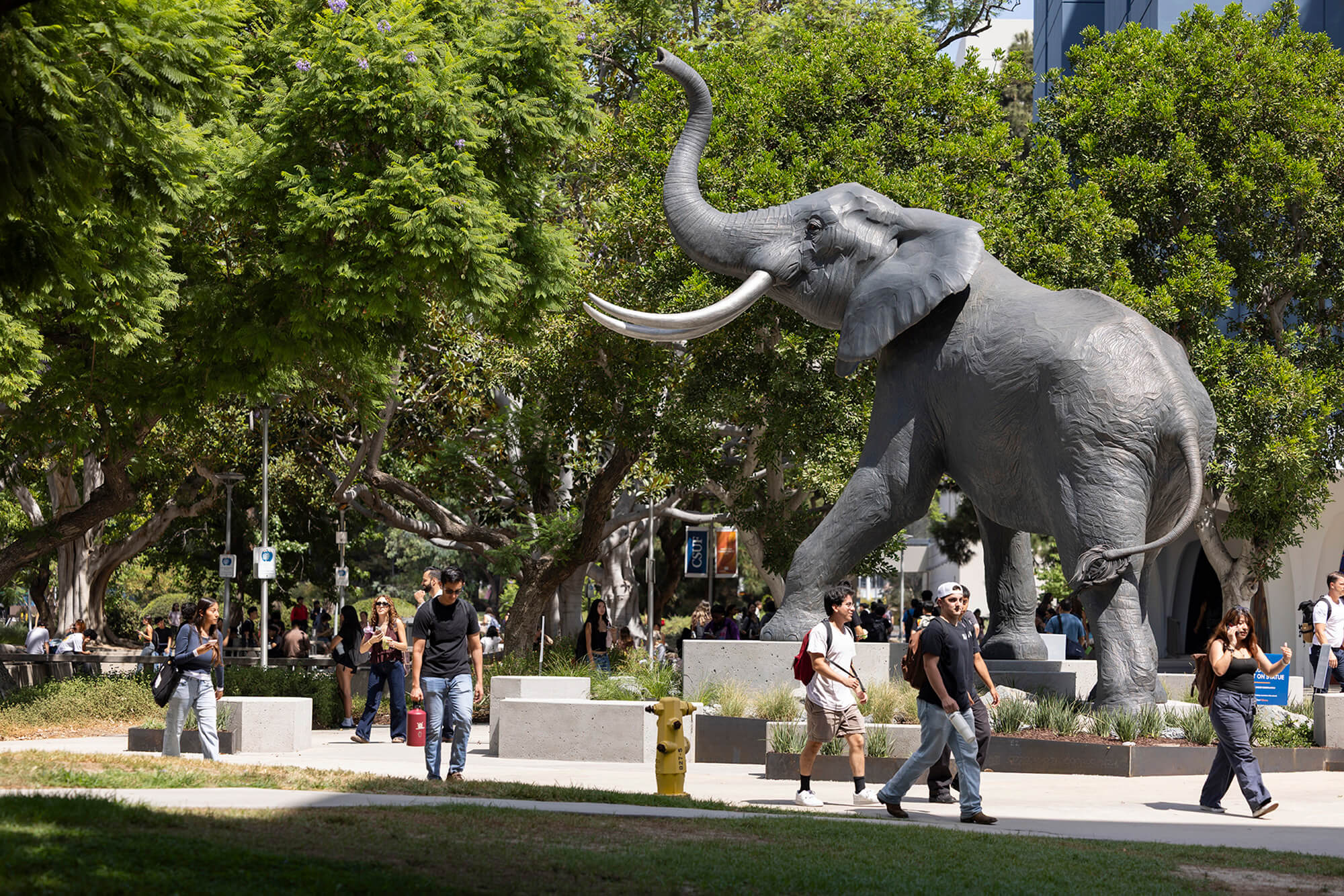 Titan the Elephant statue overlooks students walking through a tree-lined campus plaza at California State University, Fullerton.